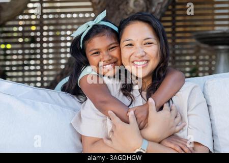 Mamma e figlia sorridenti che si abbracciano sul divano, godendosi del tempo libero insieme. Famiglia, legame, affetto, amore, felice, insieme Foto Stock