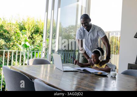 Padre afroamericano che aiuta il figlio con i compiti a casa, entrambi sorridenti felicemente. Famiglia, genitorialità, istruzione, legame, sostegno, tutoraggio Foto Stock