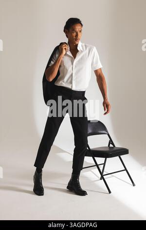 Uomo sicuro di sé in un outfit elegante che posa con una giacca in un moderno studio. Moda, stile, ritratto, sicurezza, abbigliamento da uomo, alla moda Foto Stock