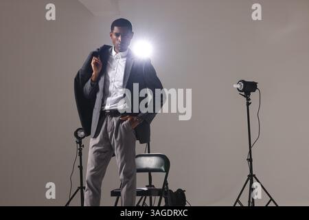 Uomo sicuro di sé in un abito elegante che posa sotto le luci dello studio, mostrando stile. stile, modellazione, abbigliamento da uomo, eleganza, ritratto, formale Foto Stock
