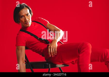 Uomo in abito rosso che posa con sicurezza sulla sedia nello studio di moda. modellazione, ritratto, creatività Foto Stock