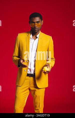 Uomo elegante in tuta gialla con limone, che posa con sicurezza in studio. Moda, sicurezza, creatività, colorato, moderno, alla moda Foto Stock
