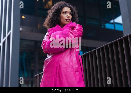 Donna sicura di sé con un cappotto rosa brillante all'aperto in un ambiente urbano moderno Foto Stock