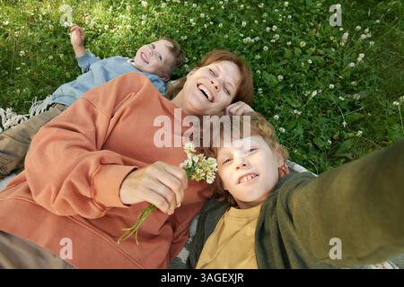POV Happy Mother e due ragazzi che scattano foto di selfie su coperta in erba Foto Stock