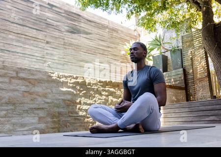 Uomo afroamericano che meditava all'aperto sul tappetino da yoga, godendosi una mattinata tranquilla. Meditazione, consapevolezza, tranquillità, relax, noi Foto Stock