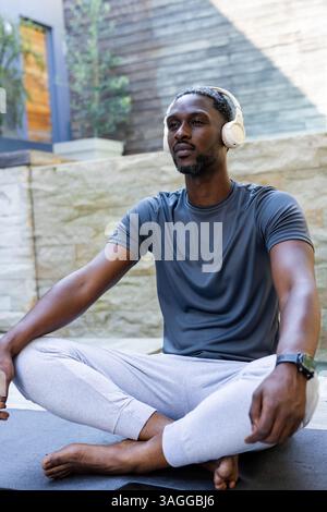 Meditando con le cuffie, un afroamericano afroamericano che si rilassa a bordo piscina nella pace mattutina. Consapevolezza, relax, tranquillità, benessere, c Foto Stock