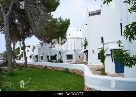 Una vista dell'architettura tradizionale di Binibeca, Minorca, caratterizzata da edifici bianchi e spazi verdi in una giornata di sole. Foto Stock