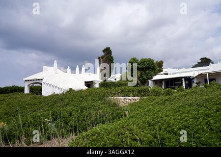 Una pittoresca vista di Binibeca, Minorca, con edifici bianchi adagiati su uno sfondo di lussureggiante vegetazione sotto un cielo coperto. Foto Stock