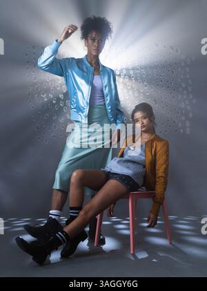 In piedi con fiducia, donna afroamericana mentre un'altra donna si siede rilassata sulla sedia. Fiducia, empowerment, diversità, amicizia, supporto, stren Foto Stock
