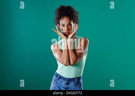 Donna afroamericana che posa con fiducia in un abito casual su sfondo verde. Ritratto, fiducia, moda, espressione, stile di vita, donna Foto Stock