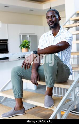 Rilassatevi a casa, un uomo afroamericano fiducioso seduto sulle scale in una cucina moderna. Stile di vita, relax, interni, tempo libero Foto Stock