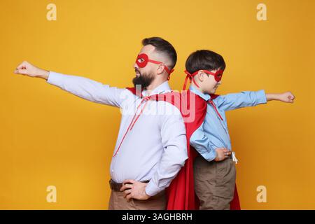 Padre e suo figlio indossano costumi da supereroe su sfondo arancione Foto Stock