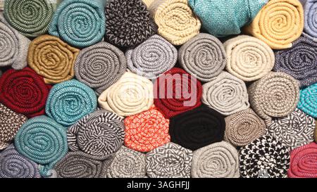 Una pila di rotoli di tessuto colorati, tra cui cashmere e altri tessuti, visti dalle estremità in un negozio di tessuti. Foto Stock