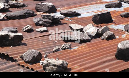Tetto in metallo ondulato fissato con pietre pesanti per evitare danni causati dal vento in un'area rurale. Foto Stock