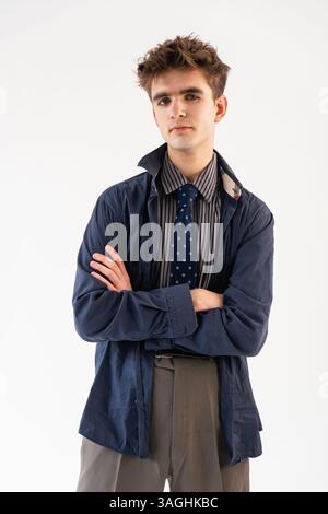 Giovane uomo con le braccia incrociate in posa in studio con camicia a righe, giacca blu e cravatta su sfondo bianco. Foto Stock