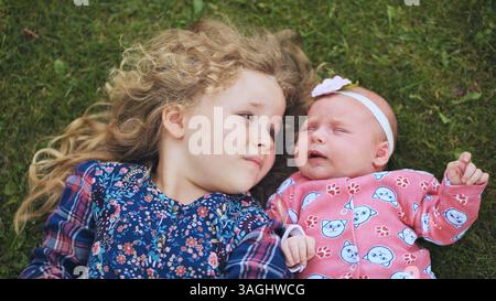 Due sorelle, un bambino giocoso e un dolce neonato, sdraiate sull'erba, godendosi una giornata gioiosa in famiglia piena di amore e risate Foto Stock