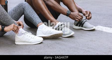 Coppia di corridori neri stringono le loro scarpe all'aperto, preparandosi per fare jogging Foto Stock