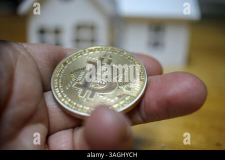 bitcoin in mano e case sfocate dietro Foto Stock