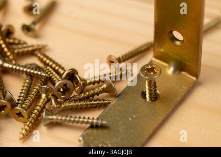 un angolo giallo con fori per il collegamento di parti in legno con viti, primo piano di prodotti da costruzione in metallo, viti sparse su una scheda Foto Stock