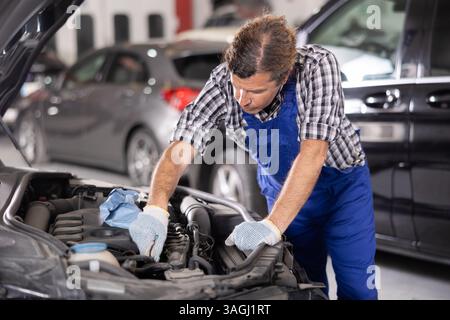 Meccanico esperto che ripara il motore di un'auto in officina Foto Stock