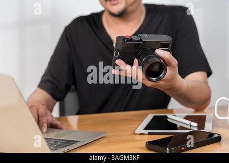 Giovane fotografo con barba che modifica le foto a casa. Fotoreporter che lavora in uno studio di agenzia. Giovane fotografo professionista impegnato nell'editing di foto Foto Stock
