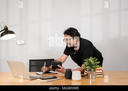 L'uomo sta modificando le foto sul computer portatile, utilizzando una tavoletta grafica e un display interattivo a penna, seduto al tavolo del caffè con una tazza di tè. Web designer in funzione Foto Stock