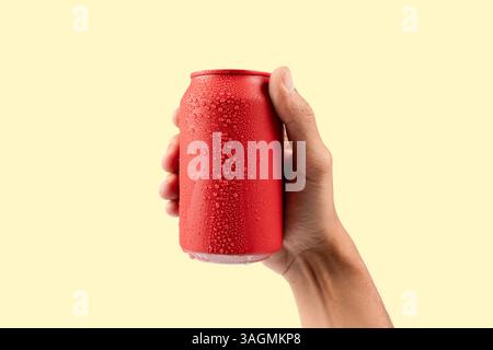 La mano maschile che tiene una bibita rossa in alluminio può simulare l'isolamento su sfondo giallo Foto Stock