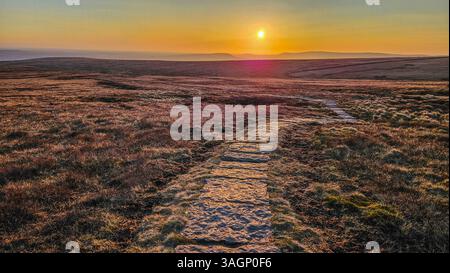 Percorso con bandiera di pietra da Pendle Summit in direzione ovest verso il tramonto primaverile. Foto Stock