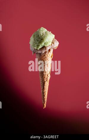 Primo piano di cono di gelato artigianale al pistacchio e alle mandorle su sfondo rosso. Concetto creativo di cibo in studio con spazio di copia, minimalista ed elegante. Foto Stock