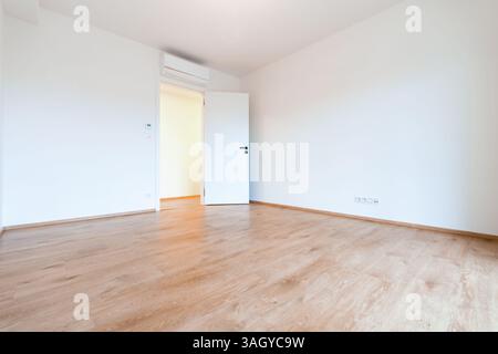 Camera vuota luminosa e ariosa in un appartamento contemporaneo, con pavimento in legno e pareti bianche Foto Stock
