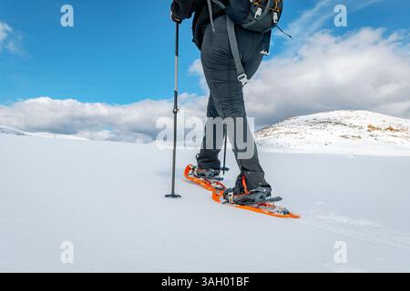 Vista posteriore ad angolo basso di una persona che cammina con le racchette da neve in una pianura innevata nella Sierra de Gredos, Spagna. Indossa pantaloni neri e racchette da neve arancioni Foto Stock