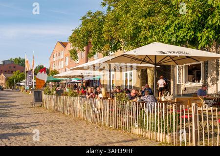 Caffetterie all'aperto lungo la strada acciottolata al molo di Orth, Fehmarn Island, Schleswig-Holstein, Germania, con persone che si godono pasti e bevande Foto Stock