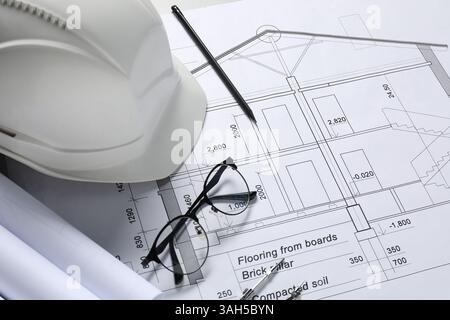 Diversi disegni architettonici, elmetto, matita, divisore e occhiali sul tavolo, primo piano Foto Stock