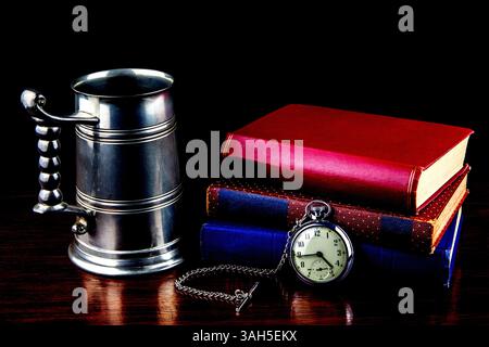 Orologio da tasca vintage con vecchia tankard in peltro e libri su una superficie in legno verniciato Foto Stock