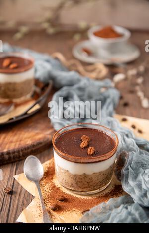 Budino di chia tiramisù in un bicchiere, ricoperto di cacao in polvere e chicchi di caffè, con uno sfondo rustico, un tessuto morbido e un cucchiaio vintage Foto Stock