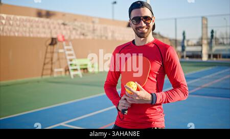 Ritratto di un uomo giovane, felice e sorridente che tiene in mano una palla da picchetto e una palla sul campo Foto Stock