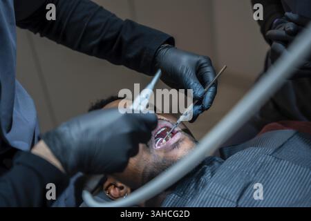 Dentista che indossa guanti neri che esaminano i denti del paziente con strumenti odontoiatrici durante il check-up in una moderna clinica odontoiatrica Foto Stock