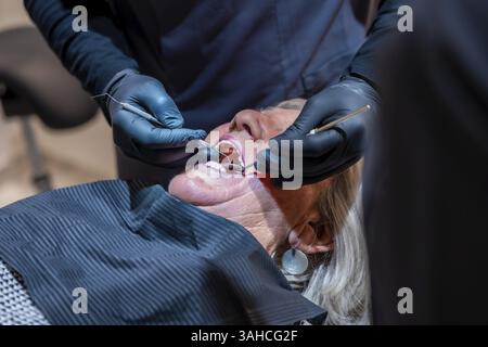 Dentista che indossa guanti neri che esaminano i denti di una paziente anziana con strumenti dentali durante l'appuntamento di controllo Foto Stock