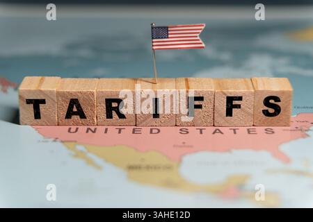 Blocchi di legno che scrivono la parola TARIFFE con una piccola bandiera statunitense posta su una mappa degli Stati Uniti. Foto Stock