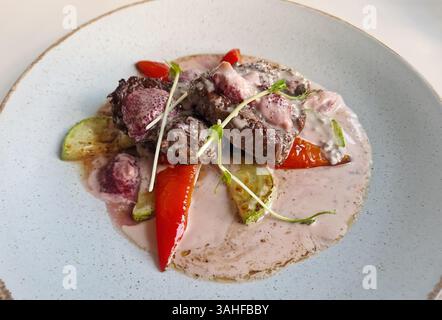 Medaglioni di bistecca di manzo alla griglia con salsa di panna bianca, fragole balsamiche, zucchine e peperone. Primo piano pasto gustoso sul tavolo in un piatto Foto Stock