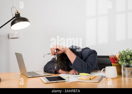 Uomo d'affari affaticato con disturbi del sonno che dorme alla scrivania. Uomo d'affari che dorme sul computer portatile alla scrivania in ufficio. Privazione del sonno e straordinari ov Foto Stock