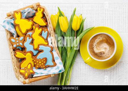 Scena di Pasqua con biscotti al pan di zenzero a forma di coniglietto, tulipani gialli e tazza da caffè Foto Stock