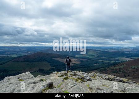 Un escursionista si erge in cima a Mither Tap nelle Bennachie Hills in Scozia, ammirando la campagna dell'Aberdeenshire che si estende in lontananza. Foto Stock