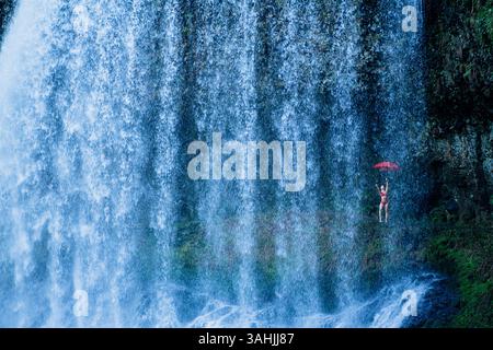 Donna con ombrello rosso in piedi vicino a una grande cascata. Silver Falls, Oregon, Stati Uniti Foto Stock