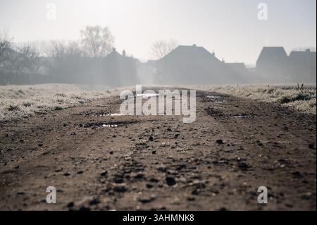 Una strada sterrata si snoda attraverso una scena pittoresca con affascinanti case annidate sullo sfondo in una giornata nebbiosa e ricoperta di nebbia Foto Stock