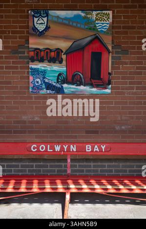 Galles del Nord. Colwyn Bay. Stazione ferroviaria. Sedile con un dipinto sul muro. Foto Stock