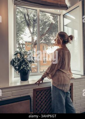 Una donna guarda fuori dalla finestra in una soleggiata giornata estiva a Odessa Foto Stock