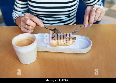 Una donna gode di una deliziosa fetta di torta al cioccolato con caffè in un caffè. Foto Stock