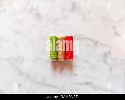 tre bobine colorate di filo su uno sfondo di marmo bianco liscio. il filo si trova al centro lasciando uno spazio sufficiente intorno al bordo Foto Stock
