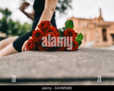 Donna seduta su una panchina con un bouquet di rose rosse in grembo. Le rose sono disposte in modo che non si tocchino l'un l'altra, e lo sono tutte Foto Stock